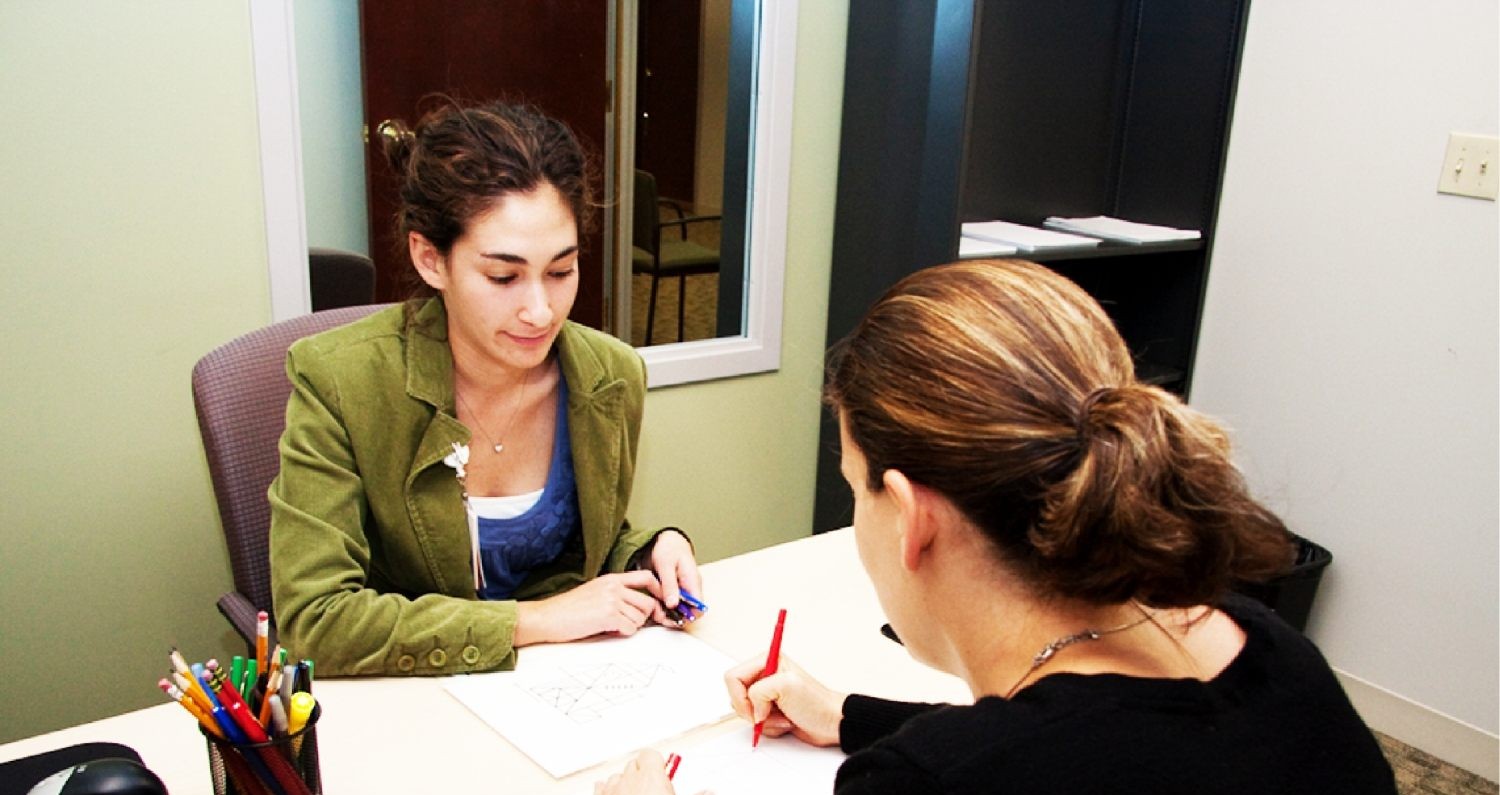 A woman signing a document with another woman.